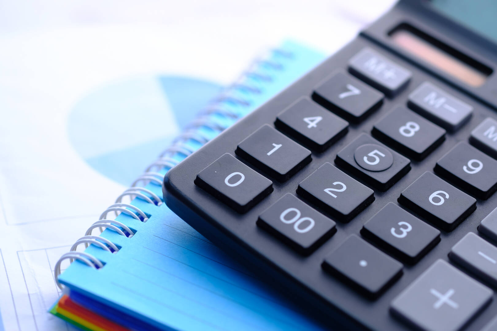 Close up of blue calculator and notepad on color background